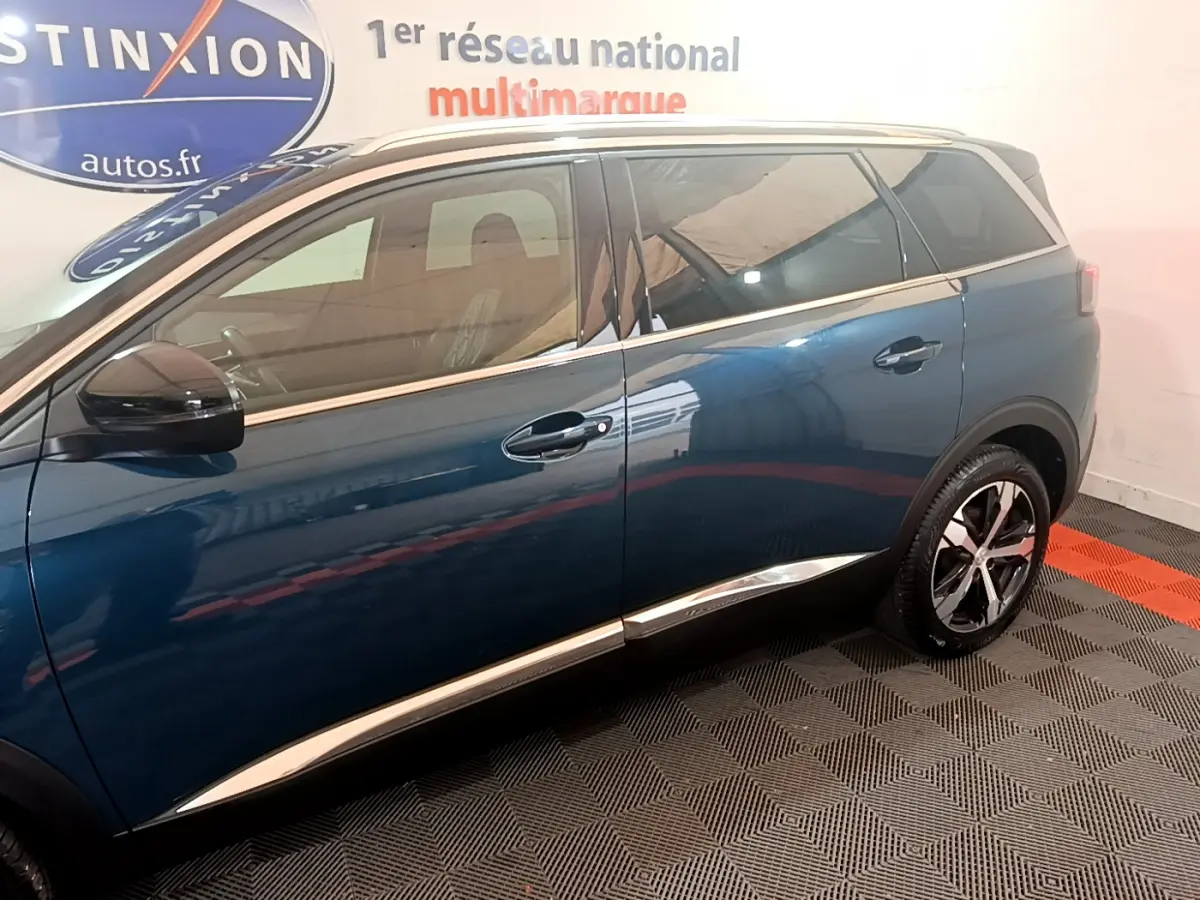 Profil côté gauche du Peugeot 5008 bleu 2021 avec jantes alliage et vitres teintées en intérieur showroom.