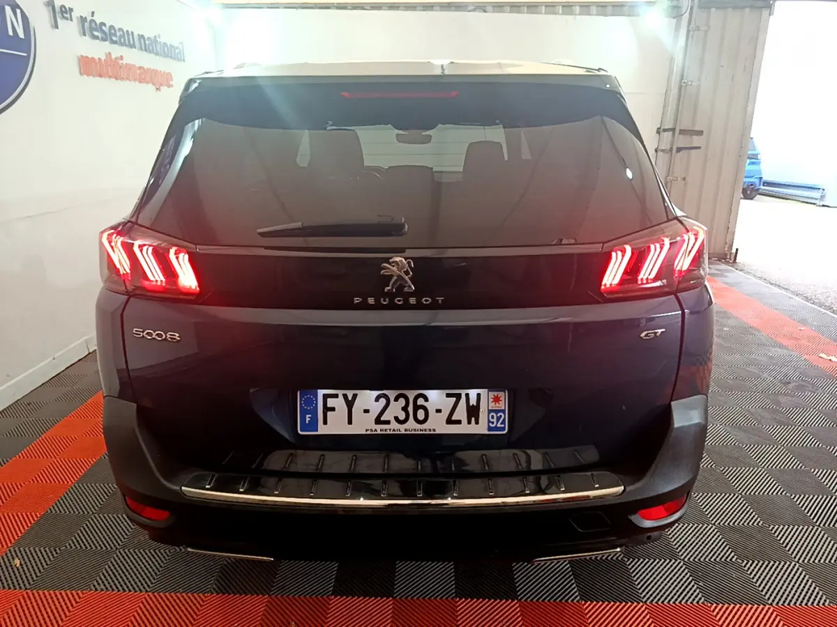 Vue arrière du Peugeot 5008 GT bleu avec feux LED caractéristiques allumés et plaque d'immatriculation française visible.