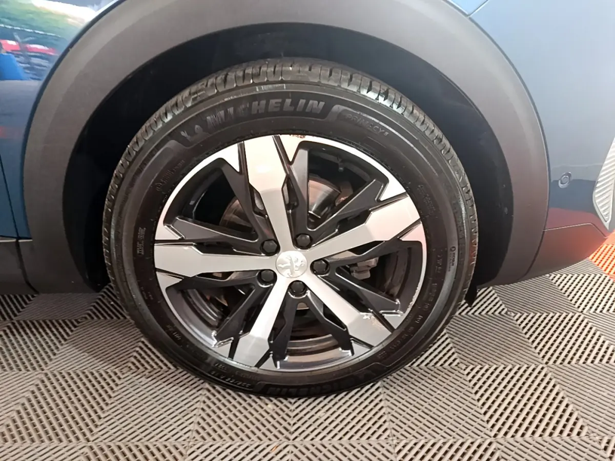 Gros plan sur la roue avant gauche du Peugeot 5008 bleu avec jante alliage bicolore et pneu Michelin.