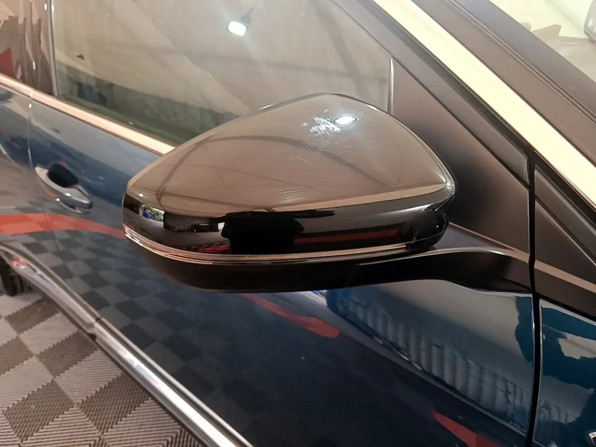 Rétroviseur noir côté gauche sur Peugeot 5008 bleu, vue rapprochée du miroir et porte avant.