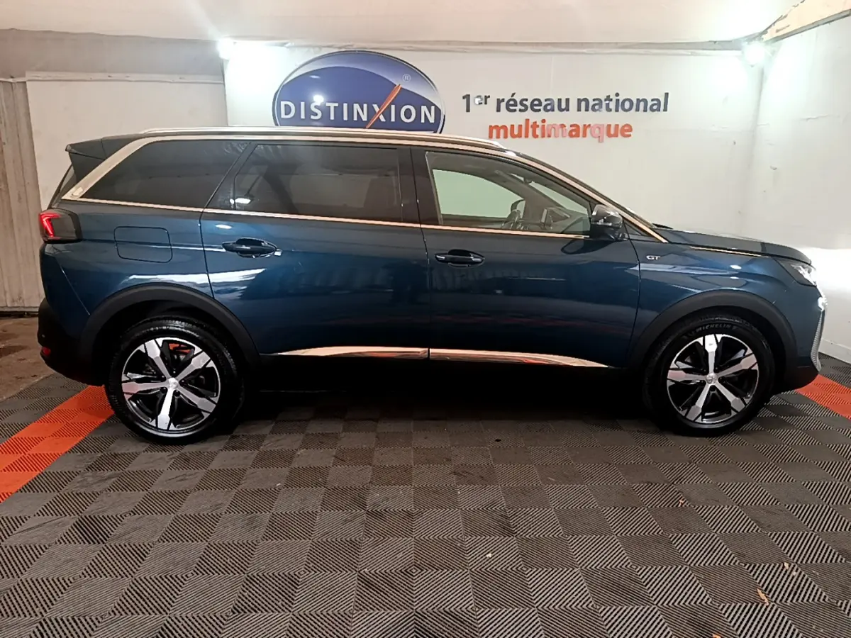 Profil droit d'un Peugeot 5008 GT bleu 2021 avec jantes alliage et toit contrasté blanc en intérieur showroom.