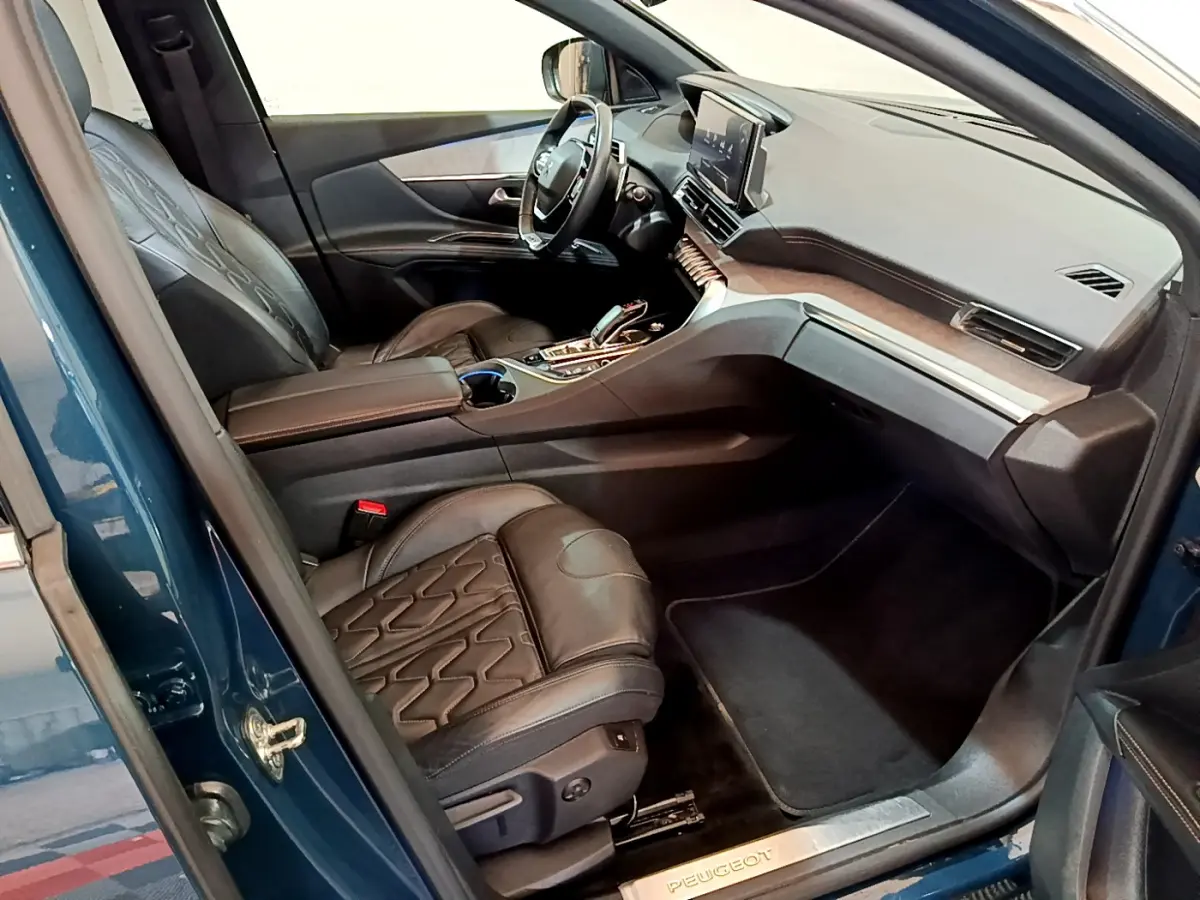 Intérieur côté conducteur du Peugeot 5008 bleu 2021, avec sièges cuir noirs et tableau de bord moderne tactile.