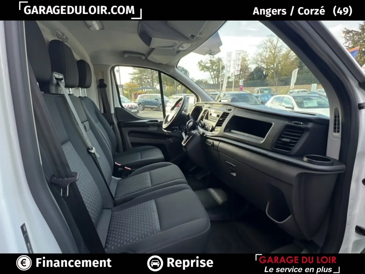 Vue intérieure côté conducteur du Ford Transit Custom blanc, montrant les sièges avant et le tableau de bord.