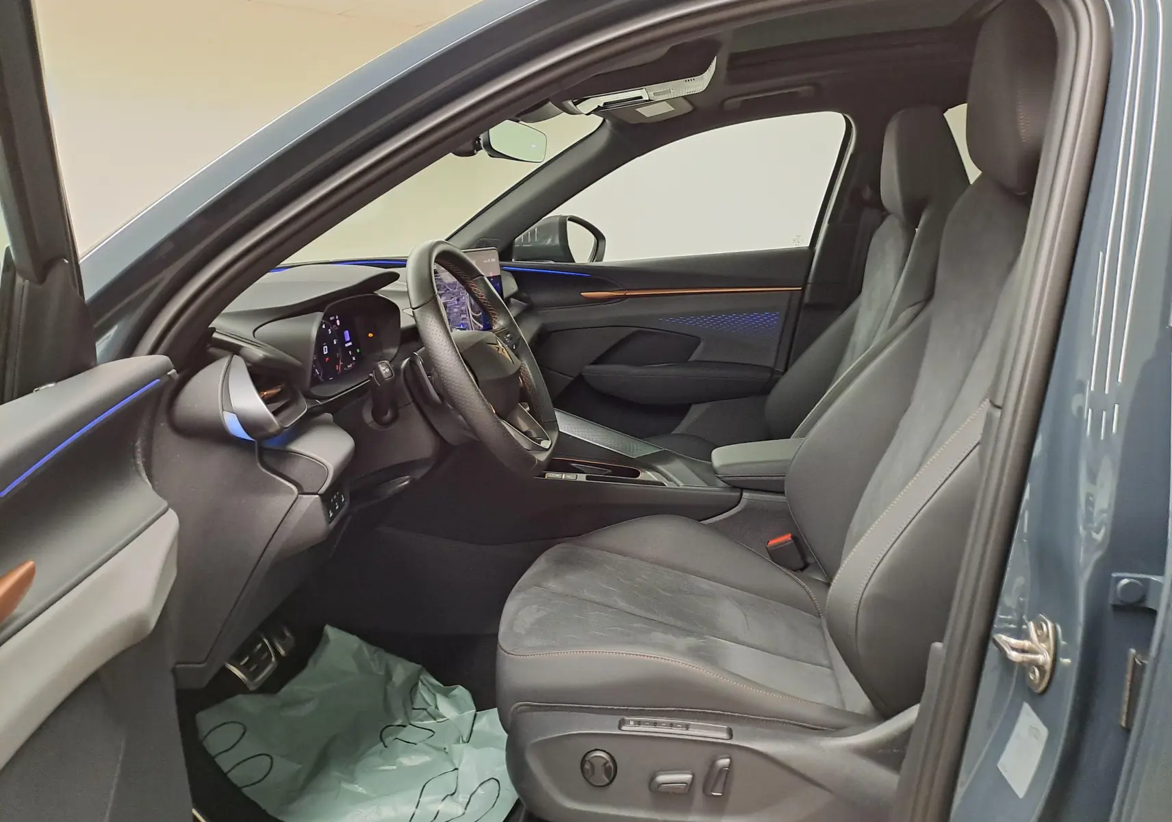 Vue intérieure côté conducteur du CUPRA TERRAMAR bleu Fjord, avec sièges en alcantara et éclairage d’ambiance bleu.