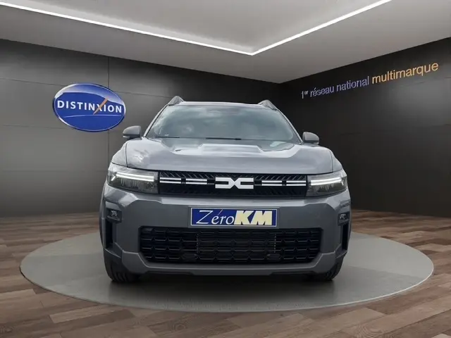 Vue de face du Dacia Bigster Journey Hybrid 155 gris foncé, avec calandre distinctive et phares LED allumés.