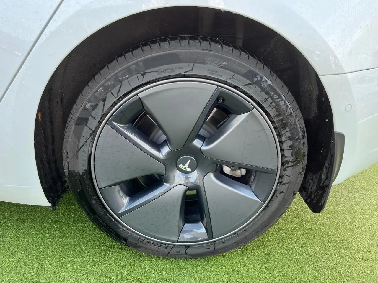 Gros plan sur la roue arrière droite d'une Tesla Model 3 blanche avec jante aérodynamique grise.