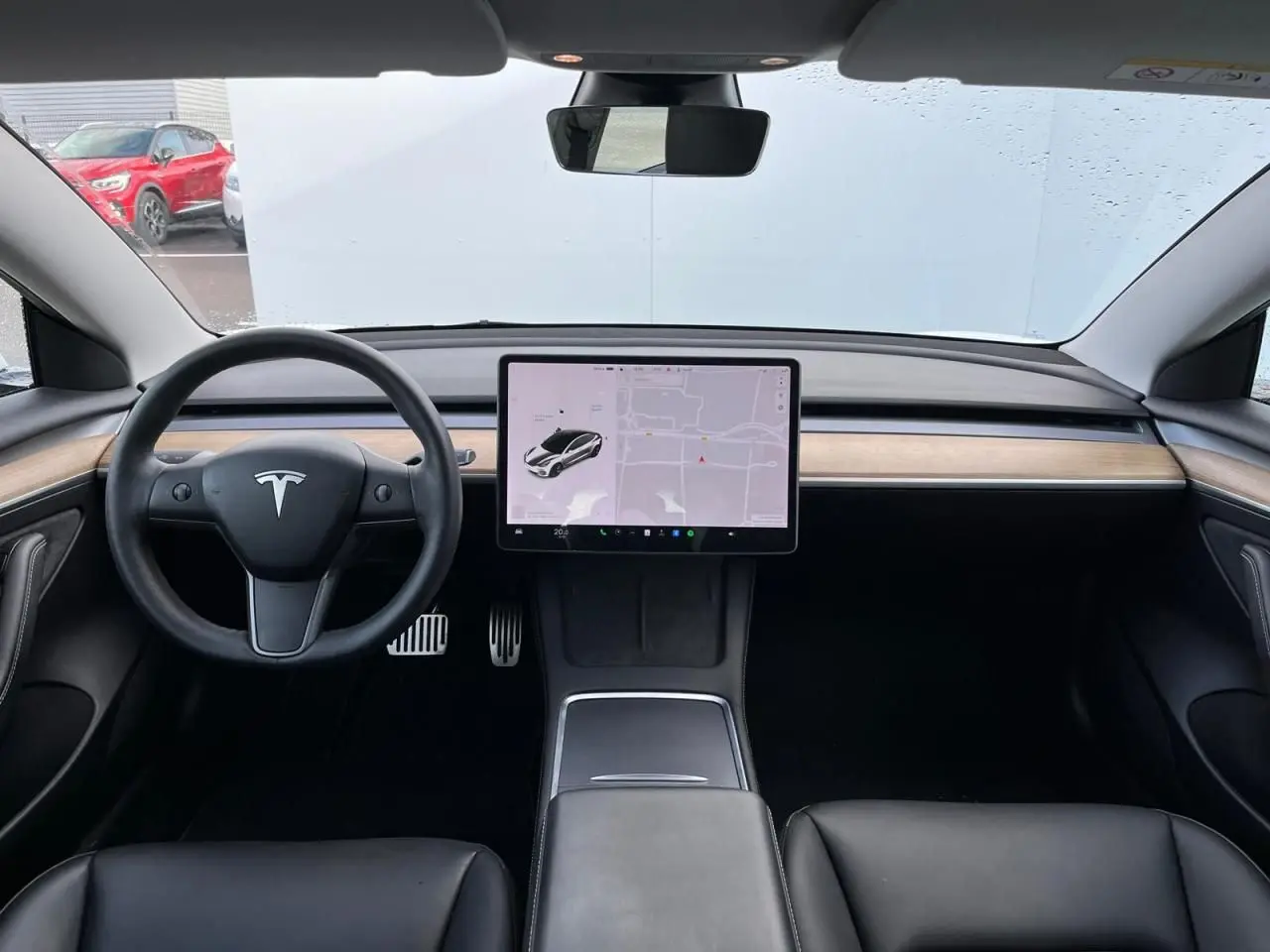 Intérieur noir et bois clair d'une Tesla Model 3 2022, vue frontale sur le tableau de bord et écran tactile central.