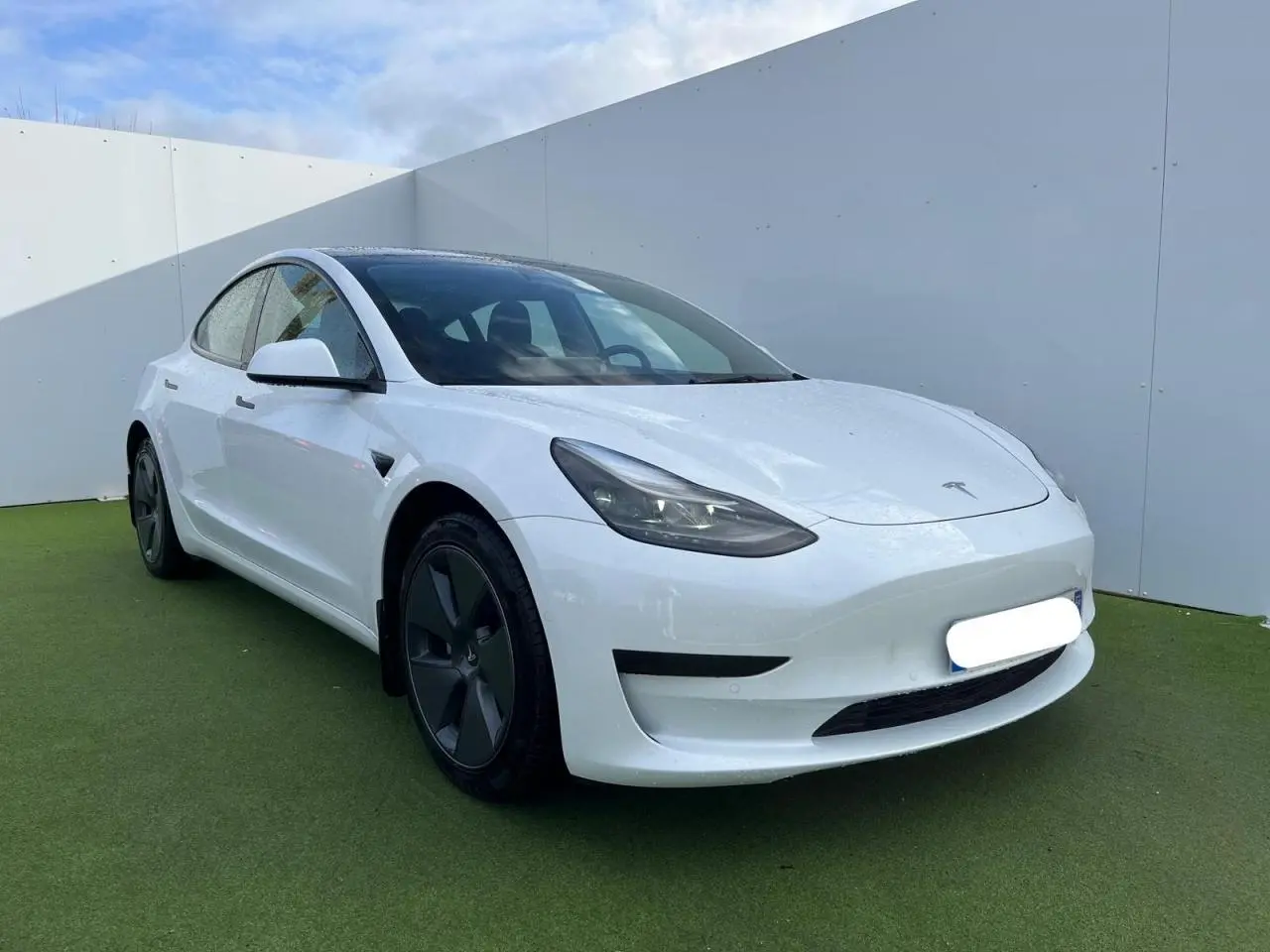 Tesla Model 3 blanc vue 3/4 avant droit, avec jantes noires et toit panoramique en verre visible.