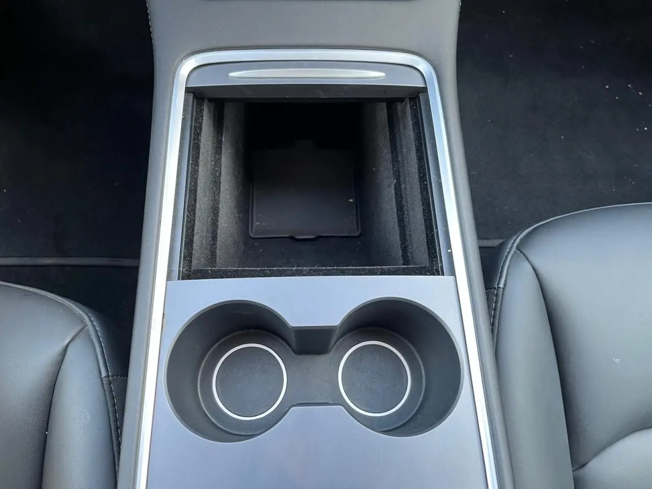 Vue plongeante sur la console centrale noire avec porte-gobelets et rangement entre les sièges avant en cuir noir.