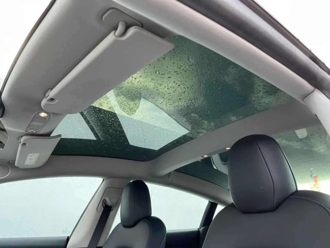 Toit panoramique en verre avec gouttes d'eau et sièges avant noirs de la Tesla Model 3 blanche vue de l'intérieur