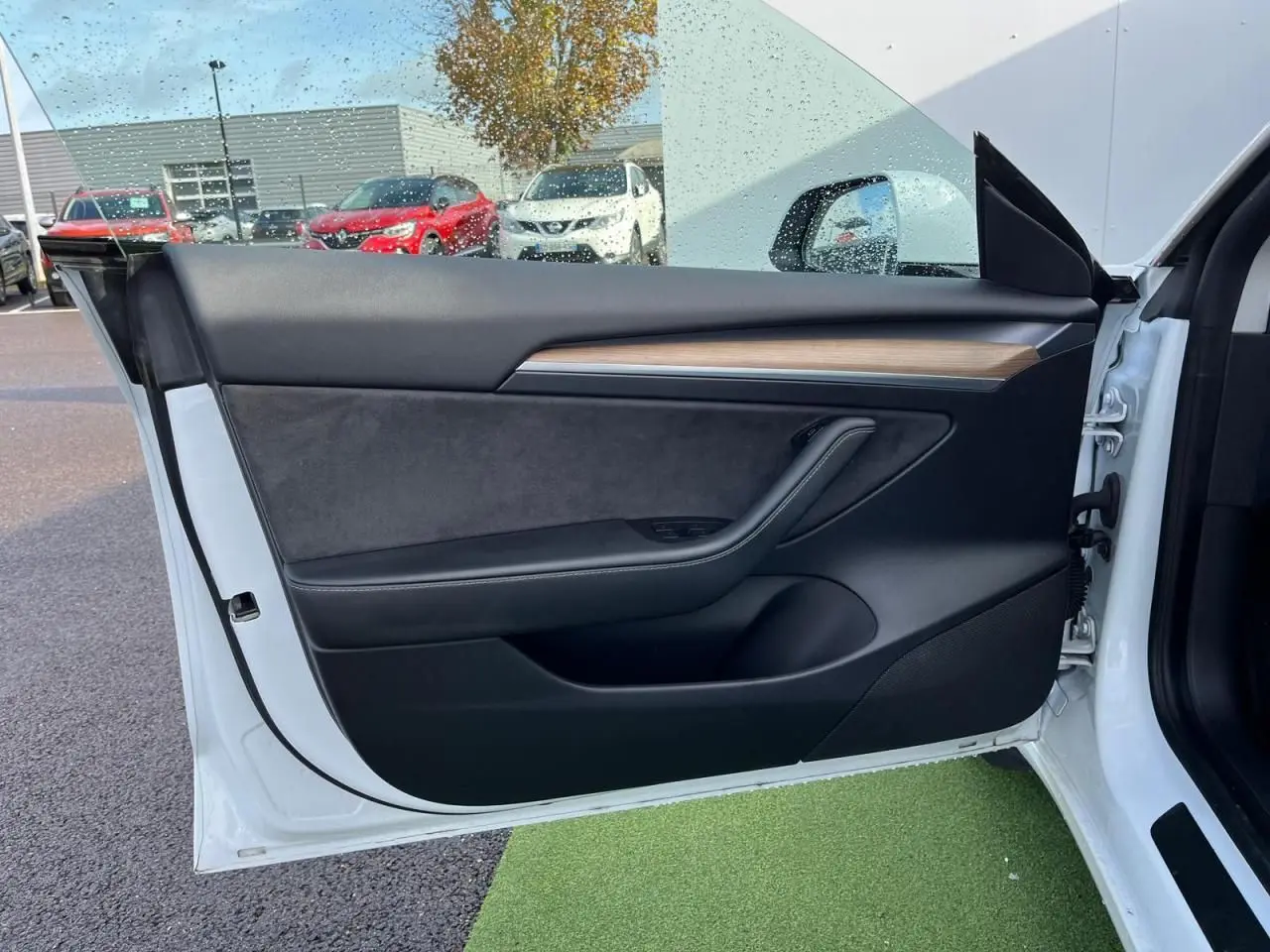 Porte avant gauche ouverte d'une Tesla Model 3 blanche, intérieur noir avec bandeau décoratif en bois.