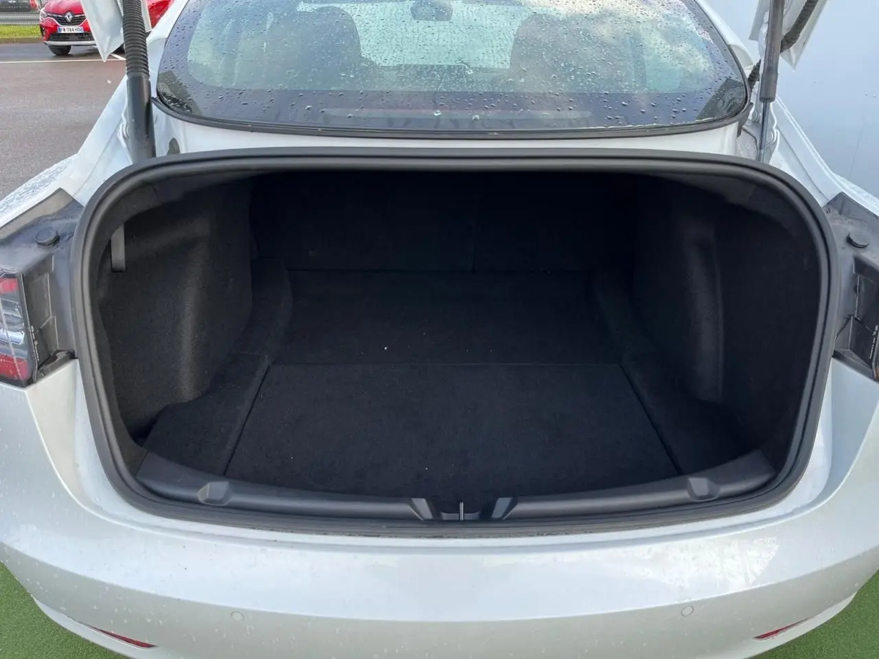 Coffre ouvert vu de l'arrière d'une Tesla Model 3 blanche 2022, intérieur spacieux et noir.