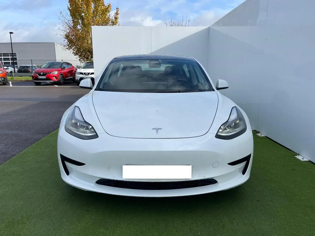 Vue frontale d'une Tesla Model 3 blanche électrique 2022, avec phares LED et capot lisse sans calandre.