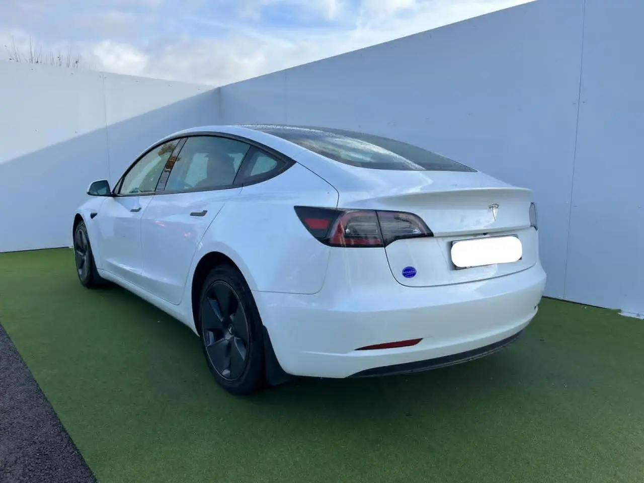 Tesla Model 3 blanc vue 3/4 arrière côté gauche, avec jantes noires et toit panoramique en verre visible.