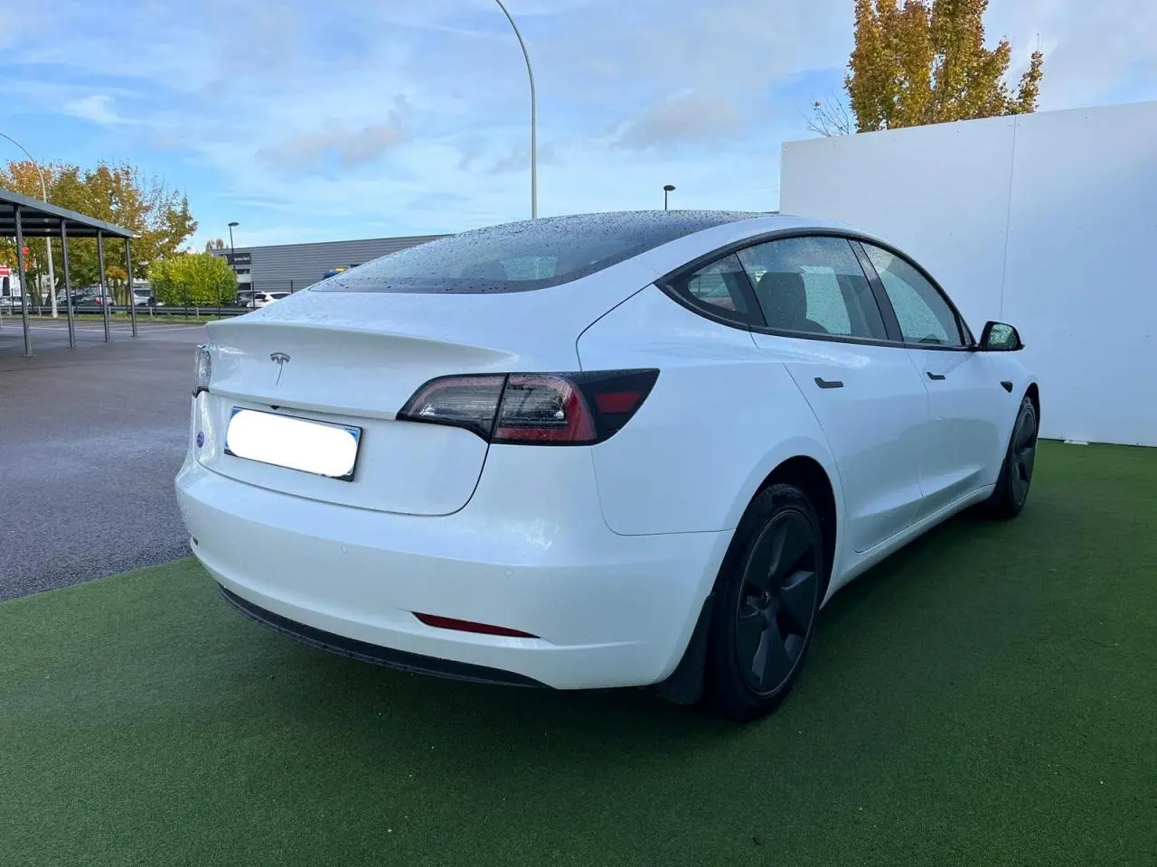 Vue 3/4 arrière droite d'une Tesla Model 3 blanche 2022 avec jantes noires et toit panoramique en verre.