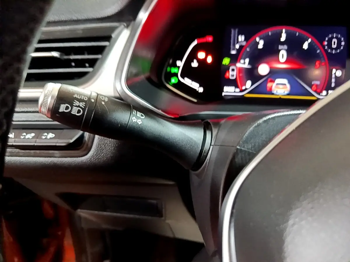 Gros plan sur la manette de commande des phares à gauche du volant avec tableau de bord numérique éclairé du Renault Captur jaune.