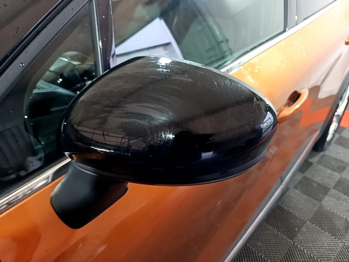 Rétroviseur noir côté gauche d’un Renault Captur jaune vu en gros plan, avec porte et poignée visibles.