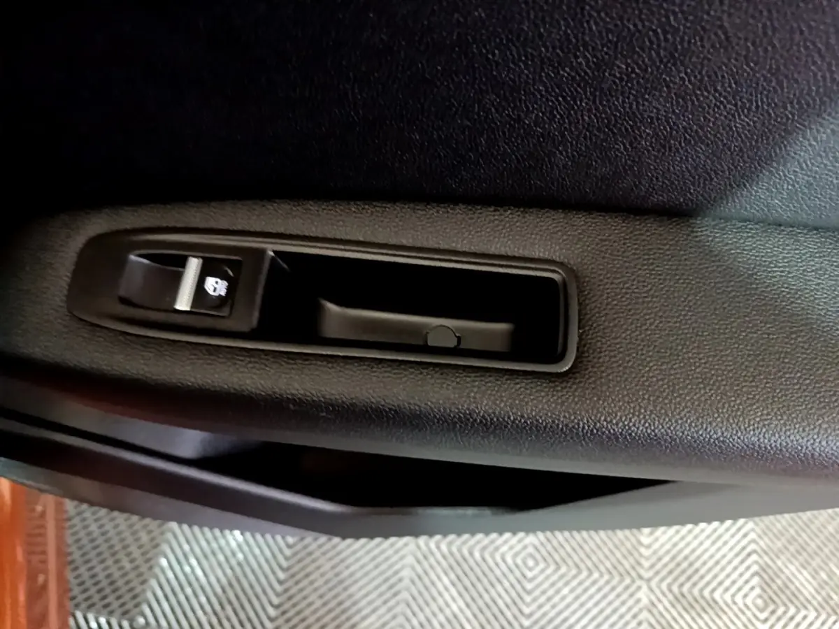 Gros plan sur la commande de verrouillage de porte noire à l'intérieur d'une Renault Captur Intens jaune, côté gauche.