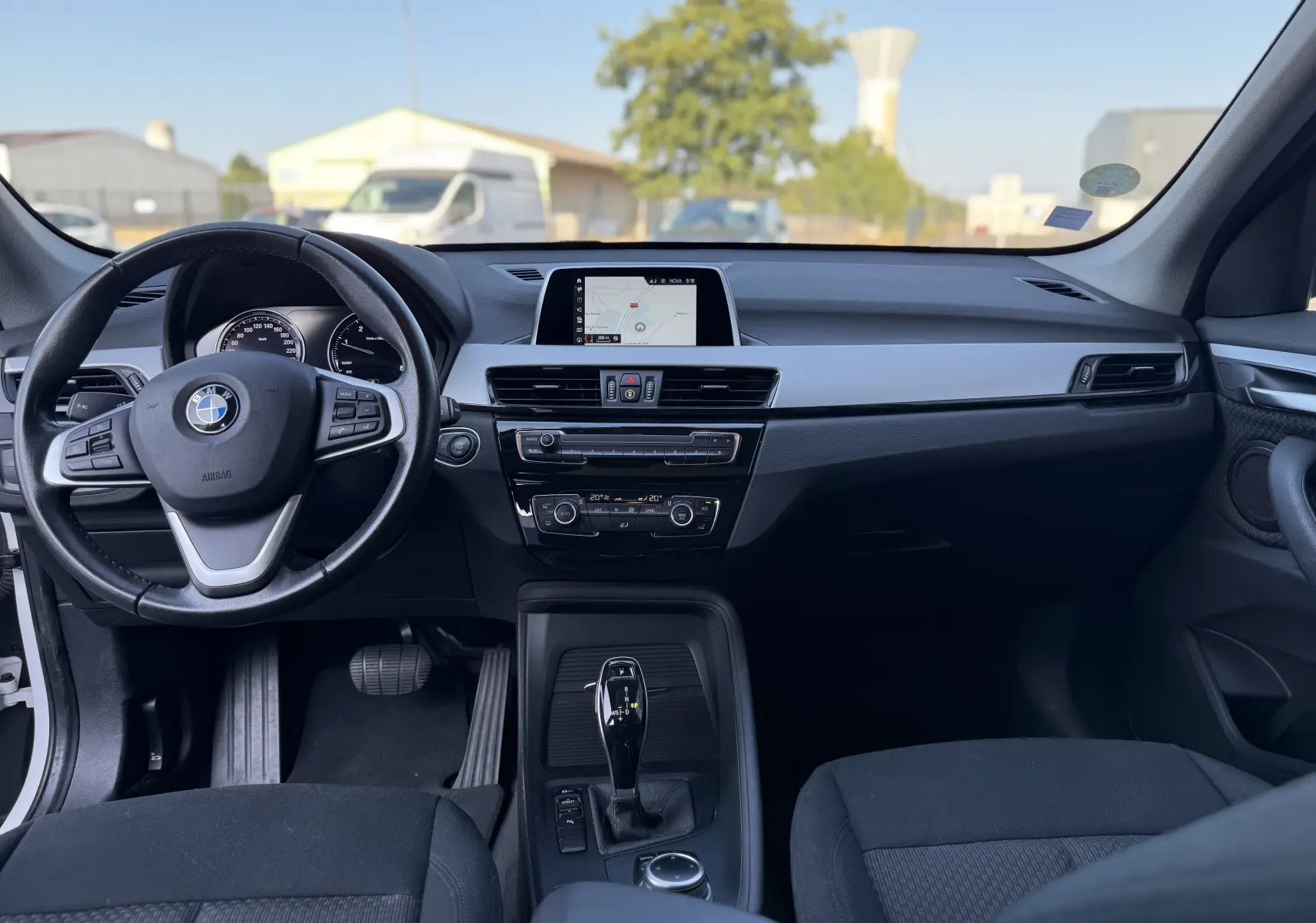 Vue intérieure avant du BMW X1 blanc 2018, montrant le tableau de bord, volant multifonction et écran central avec navigation.