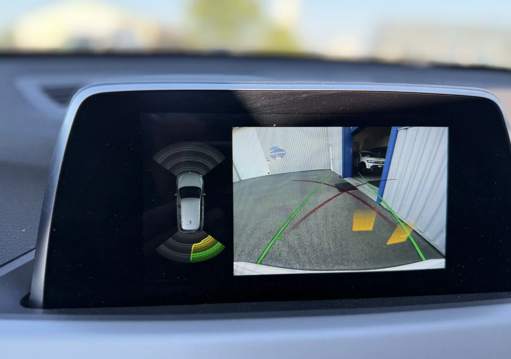 Écran de caméra de recul et capteurs de stationnement du BMW X1 blanc, vue intérieure du tableau de bord.