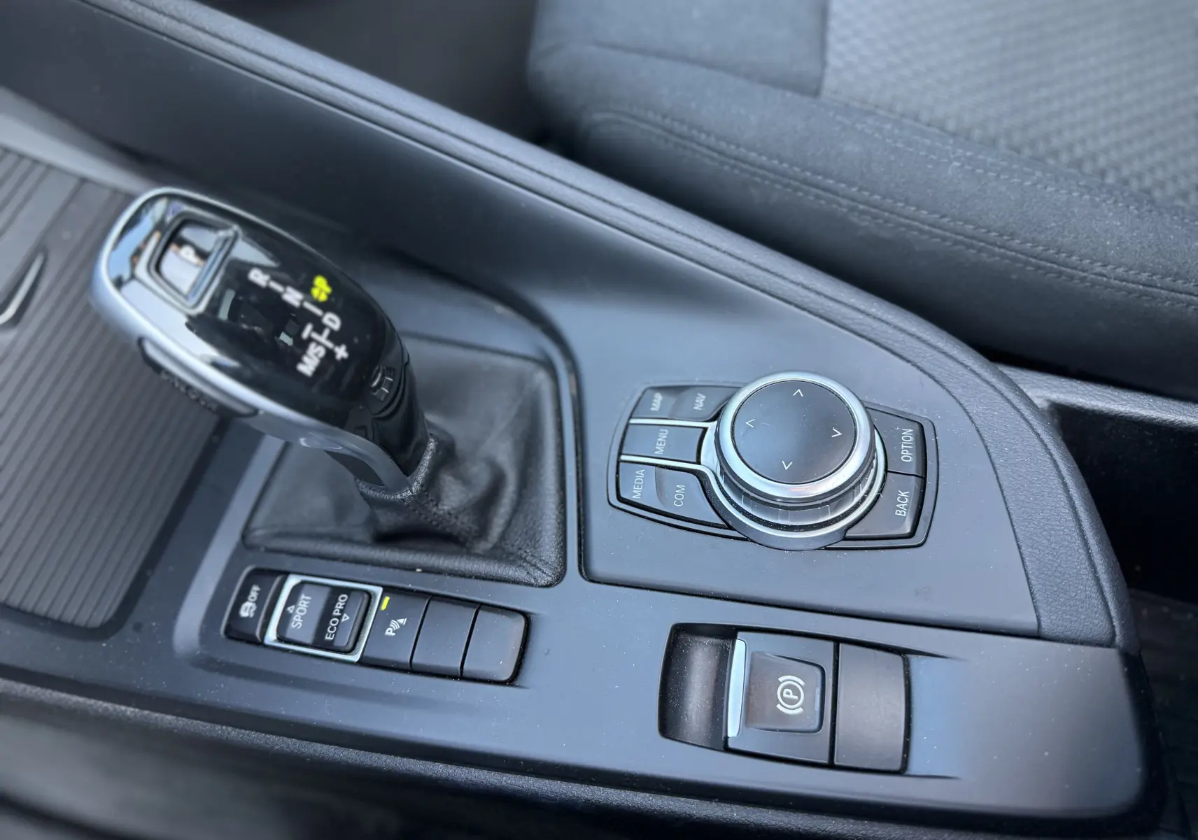 Gros plan sur la console centrale noire du BMW X1 blanc, montrant le levier de vitesse automatique et la molette de commande.