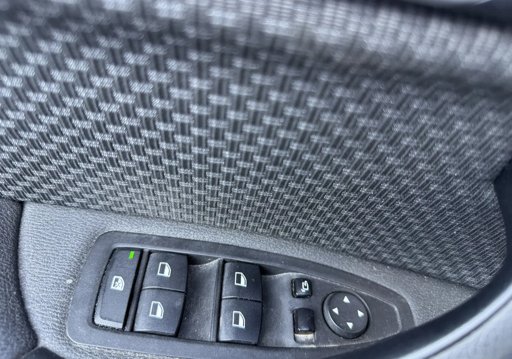 Gros plan sur les commandes des vitres électriques et rétroviseurs côté conducteur d’un BMW X1 blanc de 2018.