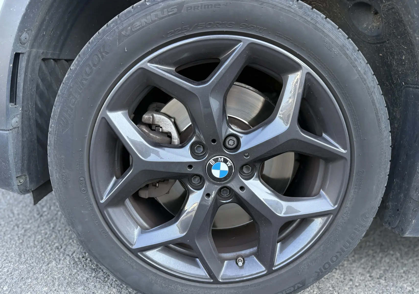 Gros plan sur la roue avant gauche d’un BMW X1 blanc, jante alliage gris foncé à cinq branches doubles.