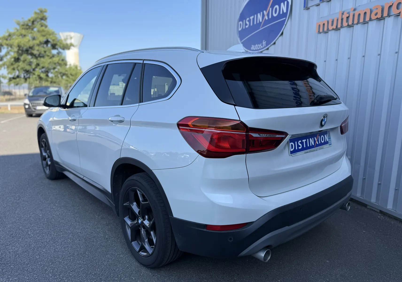 BMW X1 20D blanc vue 3/4 arrière droit, avec jantes noires et feux arrière LED distinctifs.