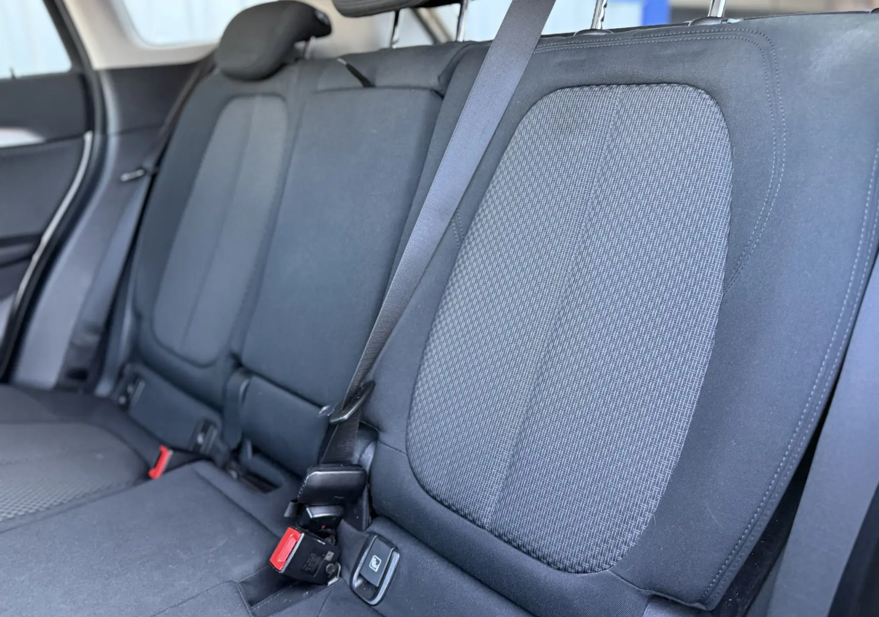 Vue rapprochée des sièges arrière en tissu noir du BMW X1 20D blanc, montrant les ceintures de sécurité et appuie-têtes.