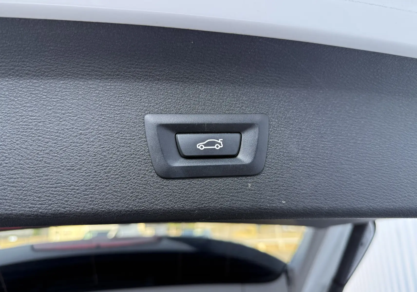 Bouton de fermeture électrique du hayon sur la partie intérieure d’un BMW X1 blanc, vue rapprochée.