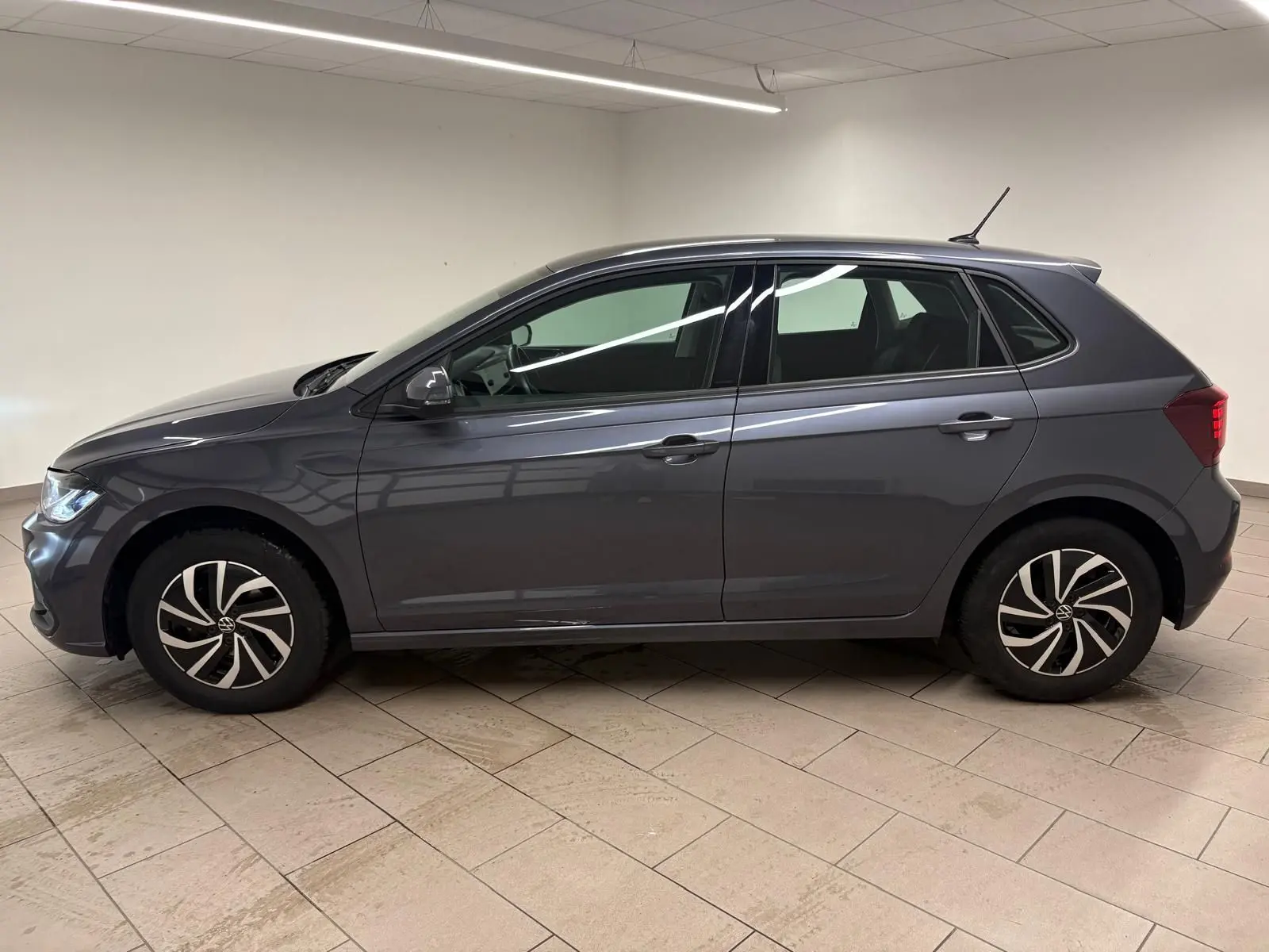 Volkswagen Polo gris cendre vue de profil côté gauche, avec jantes alliage au design distinctif, en intérieur showroom.