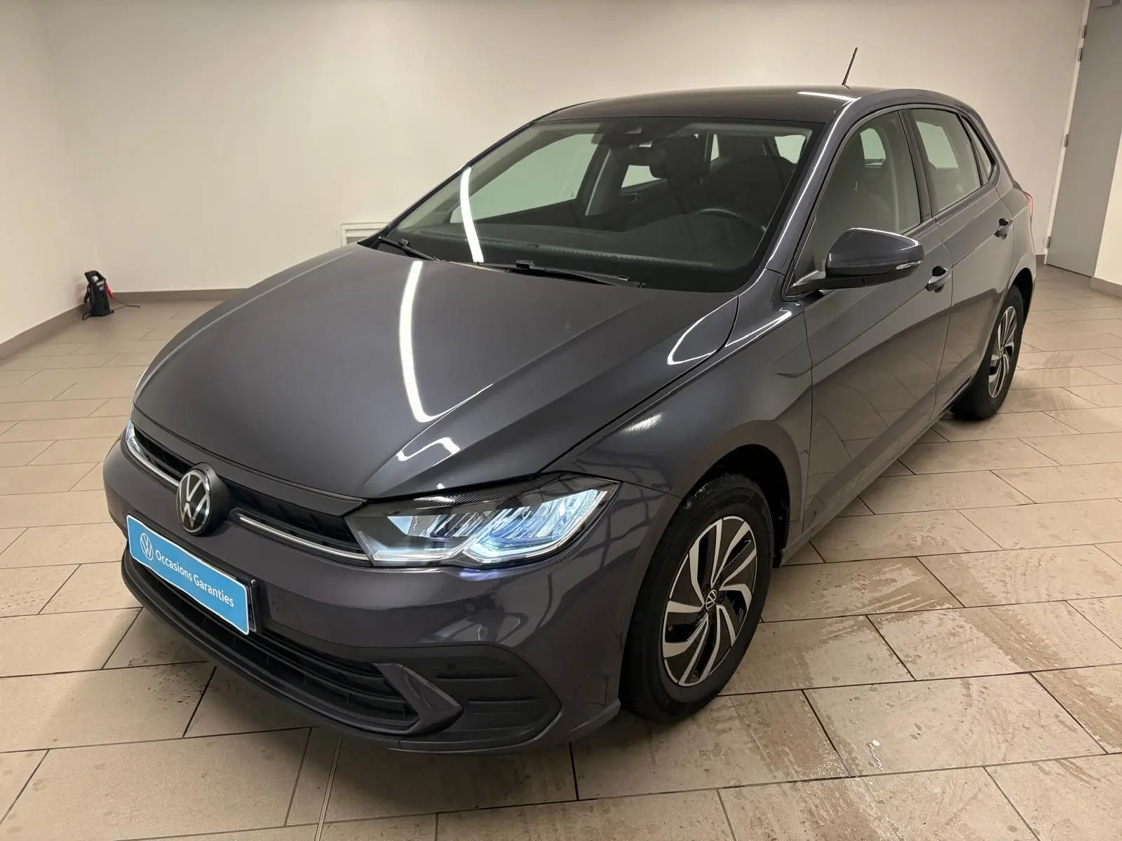 Volkswagen Polo gris cendre 2024 vue 3/4 avant droit avec phares allumés et jantes distinctives.