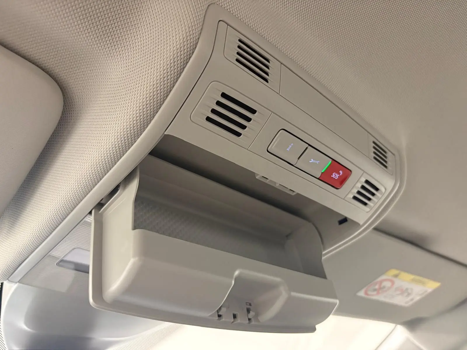 Vue intérieure du rangement lunettes ouvert au plafond d'une Volkswagen Polo gris cendre 2024, avec commandes SOS visibles.