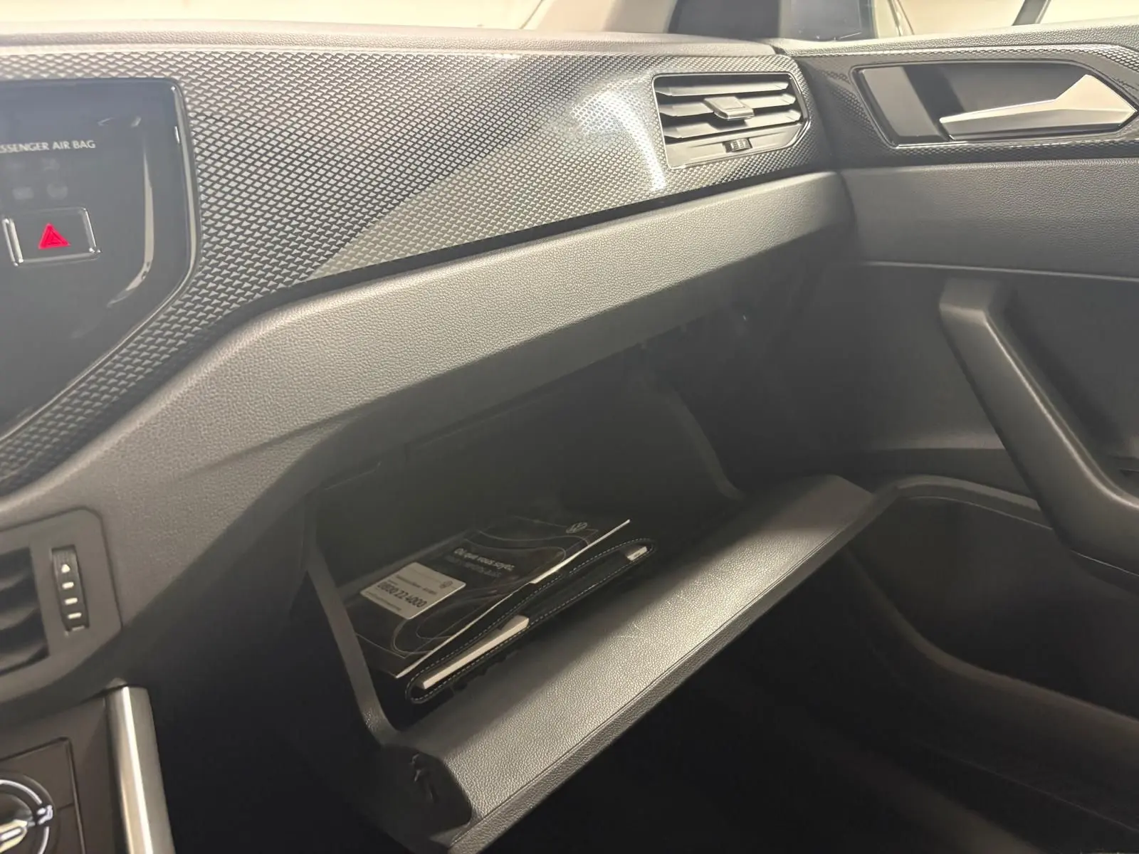 Intérieur de la Volkswagen Polo 2024 gris cendre, vue côté passager sur la boîte à gants ouverte avec documents visibles.