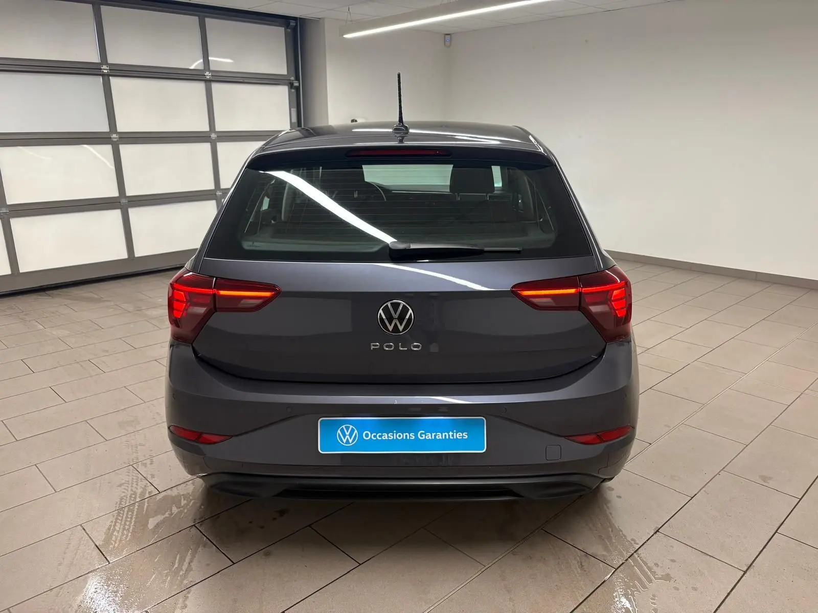 Vue arrière d'une Volkswagen Polo gris cendre 2024, avec feux arrière allumés dans un garage lumineux.