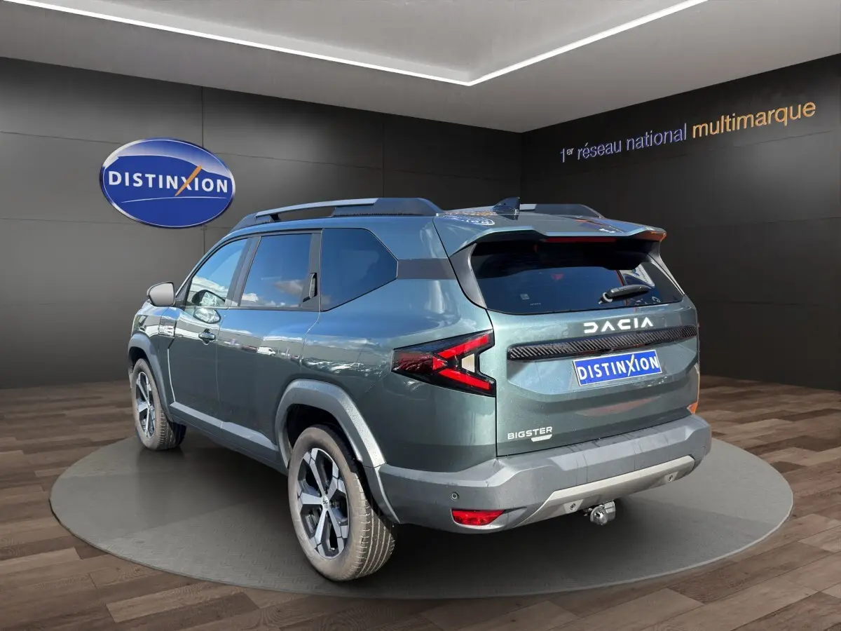 Vue 3/4 arrière droite du Dacia Bigster vert avec attelage RDSO, feux LED et jantes alliage visibles en showroom.