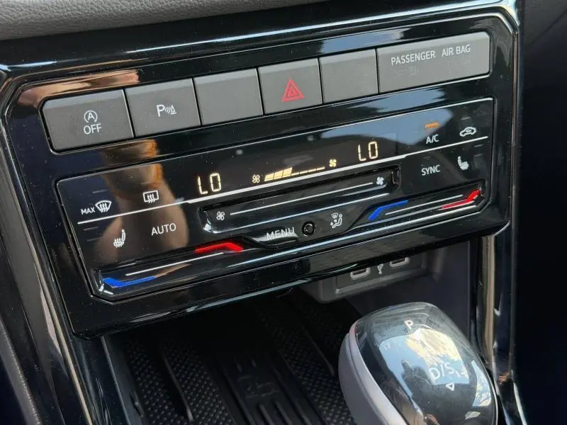 Gros plan sur la console centrale noire du Volkswagen T-Cross jaune, affichant la climatisation automatique et le levier de vitesse.