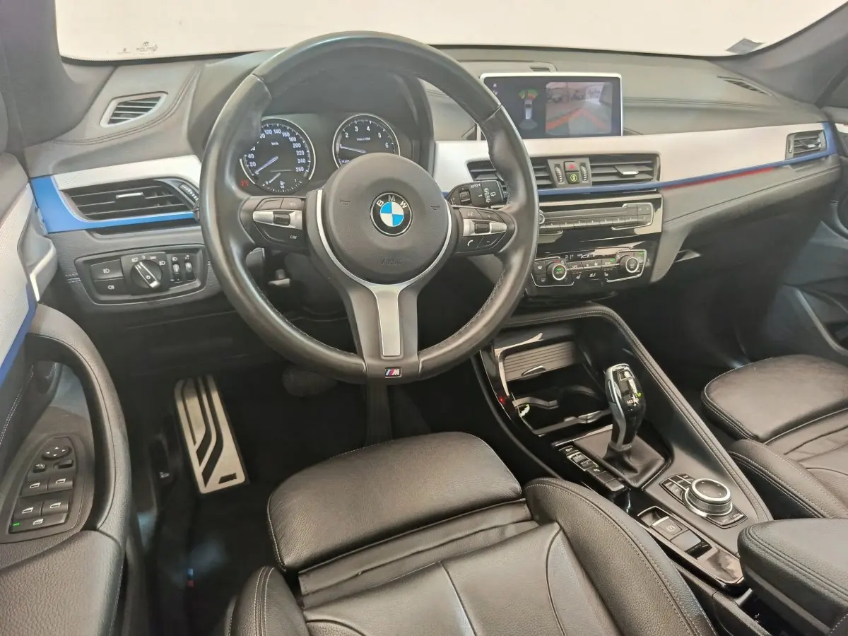 Vue intérieure avant du BMW X1 sDrive18i M Sport 2019, volant cuir, tableau de bord avec écran tactile et détails bleus.