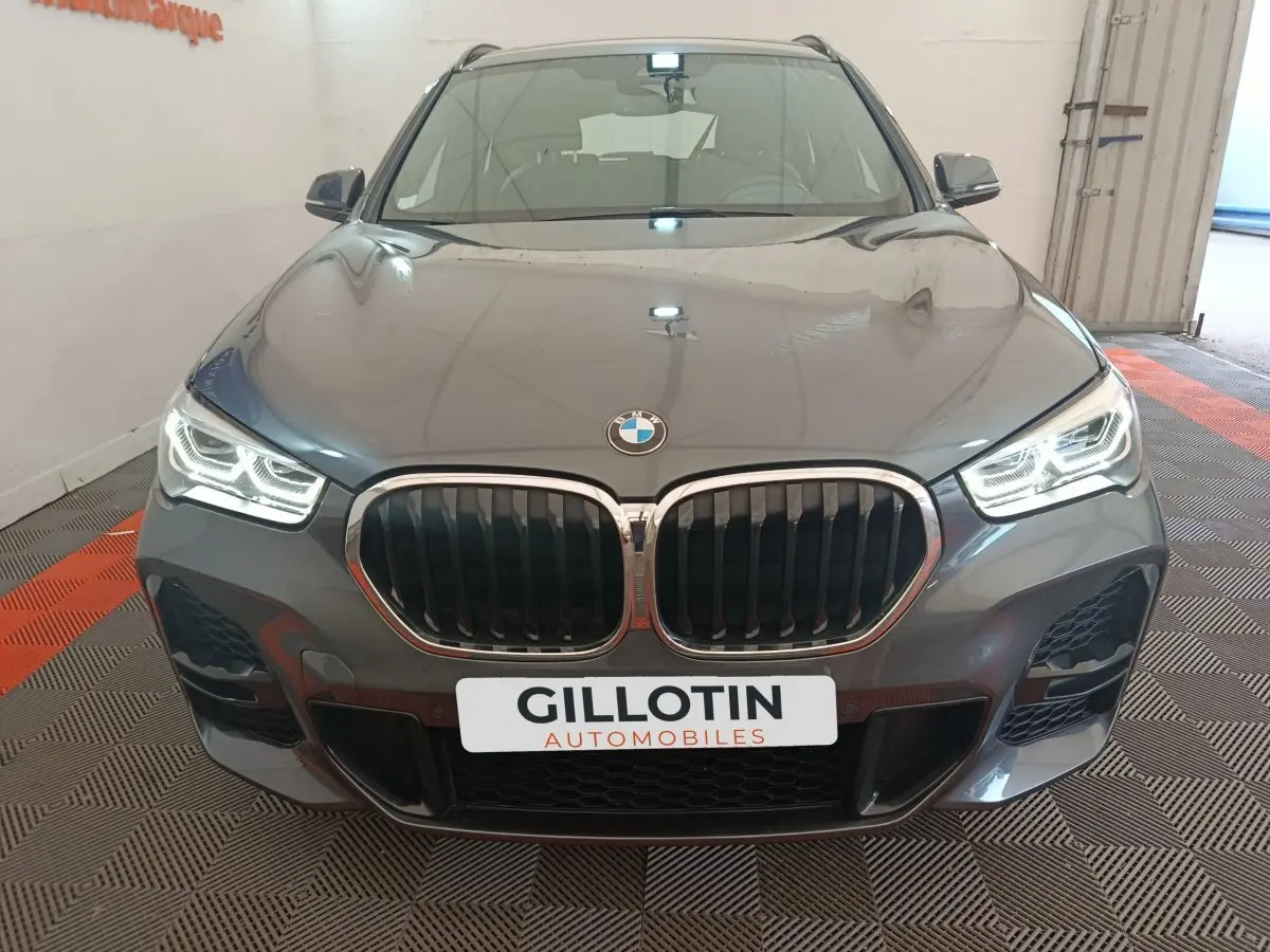 Vue frontale d'un BMW X1 sDrive18i M Sport gris métallisé avec phares LED allumés dans un garage.