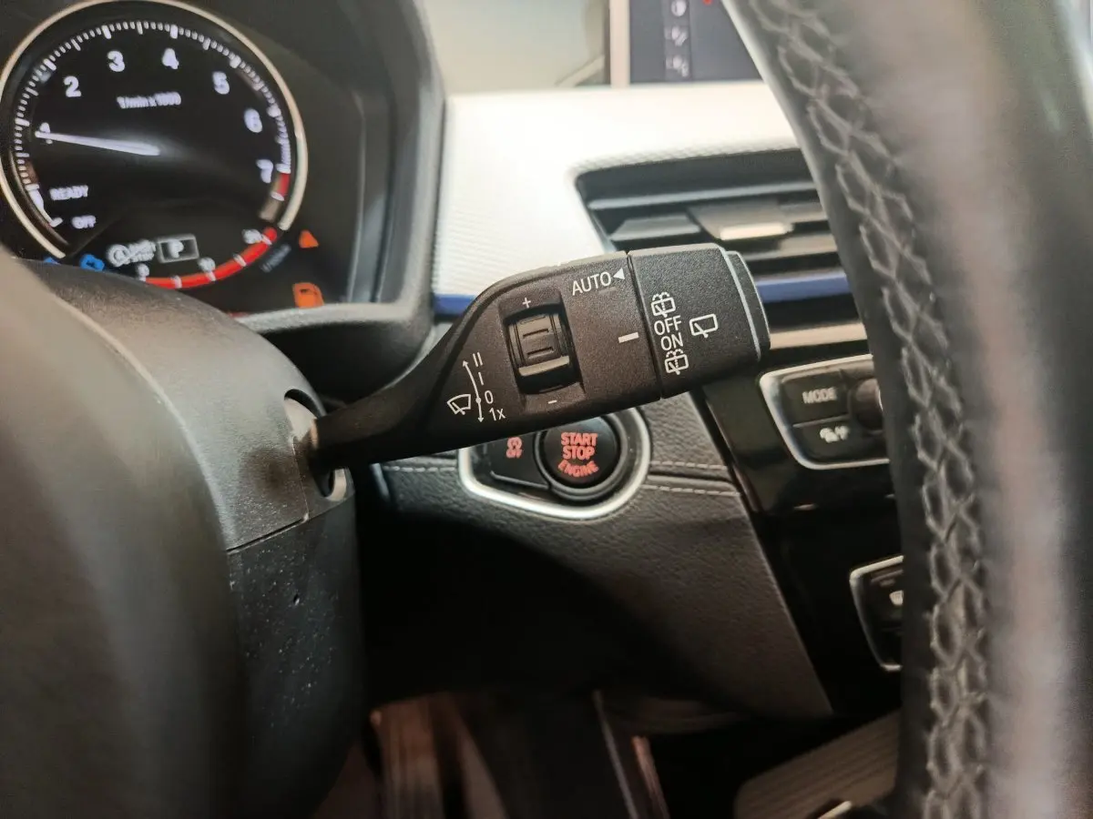 Gros plan sur la commande d'essuie-glace et le bouton start/stop du tableau de bord noir d'une BMW X1 sDrive18i M Sport 2019.