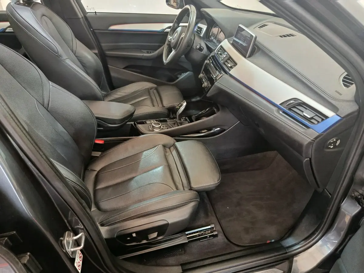 Intérieur BMW X1 sDrive18i M Sport 2019 vu côté conducteur, sièges cuir noirs et tableau de bord avec écran tactile.