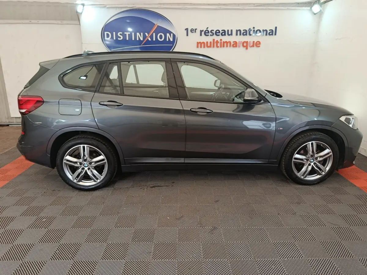 BMW X1 sDrive18i M Sport gris métallisé vu de profil côté gauche dans un showroom multimarque