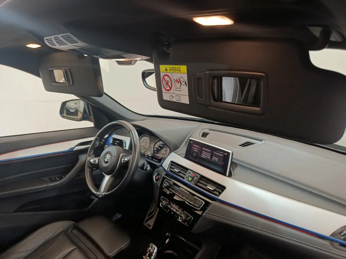 Intérieur BMW X1 sDrive18i 2019 vu côté conducteur, tableau de bord noir avec écran tactile et volant cuir.