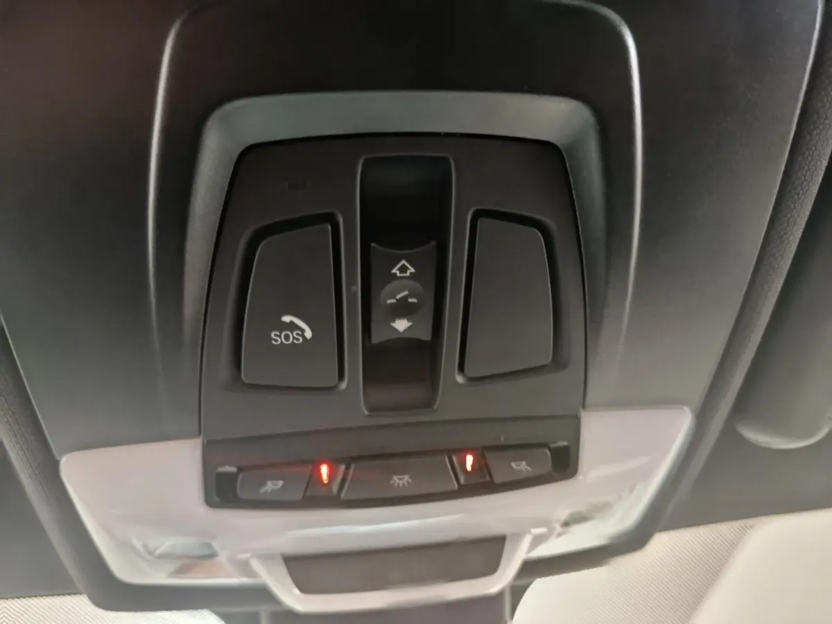 Vue en gros plan du panneau de commandes au plafond intérieur du BMW X1 sDrive18i M Sport 2019, avec bouton SOS et éclairage activé.