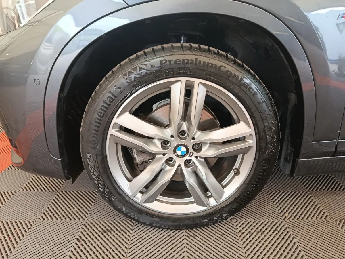 Gros plan sur la roue avant gauche grise d’un BMW X1 sDrive18i M Sport avec jante alliage et logo BMW visible au centre.