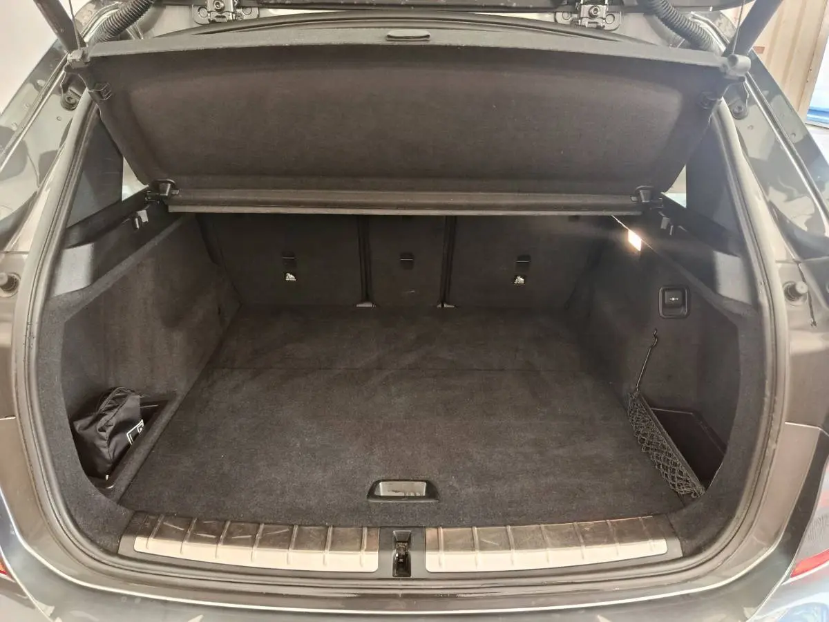 Coffre ouvert vu de l'arrière d'un BMW X1 sDrive18i M Sport 2019 gris foncé avec tapis noir et filet latéral.