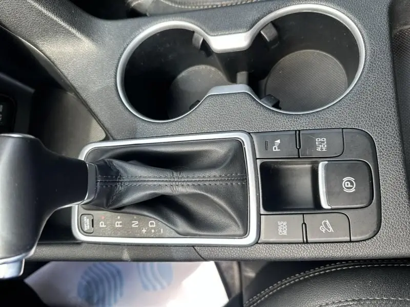 Gros plan sur la console centrale du KIA SPORTAGE 2021 avec levier de vitesse automatique et boutons de contrôle en cuir noir.
