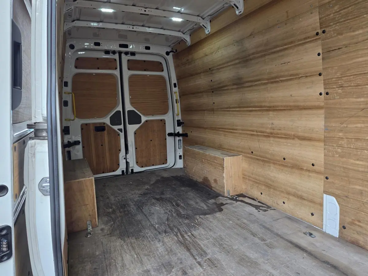 Intérieur du fourgon Volkswagen Crafter blanc vu de l'arrière, avec plancher et parois en bois clair.
