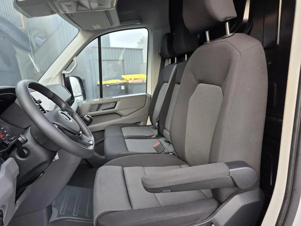 Vue intérieure côté conducteur du Volkswagen Crafter blanc 2023, sièges tissu gris avec accoudoir et volant multifonctions.