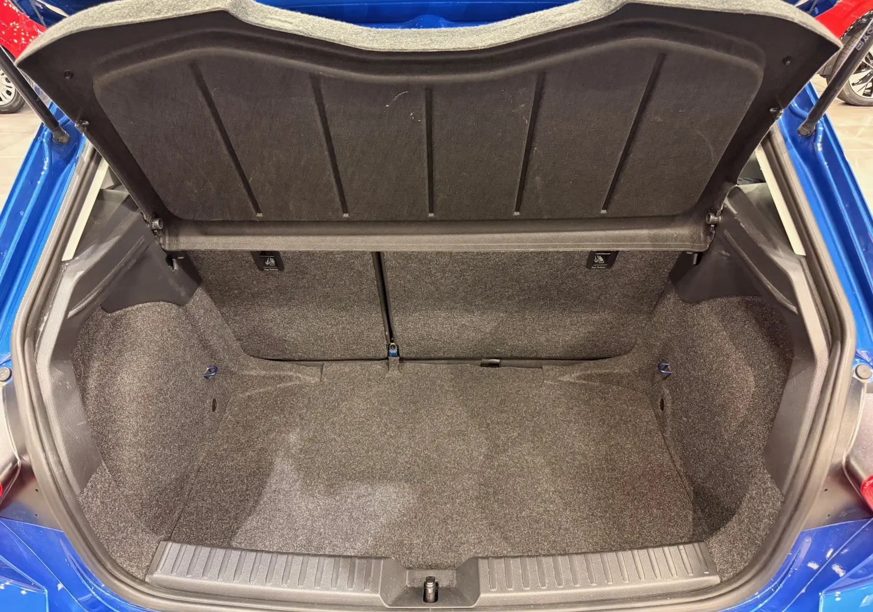 Coffre ouvert vu de l'arrière d'une SEAT Ibiza 1.0 TSI 95CH Copa bleu 2025, montrant l'espace de rangement vide et la doublure grise.